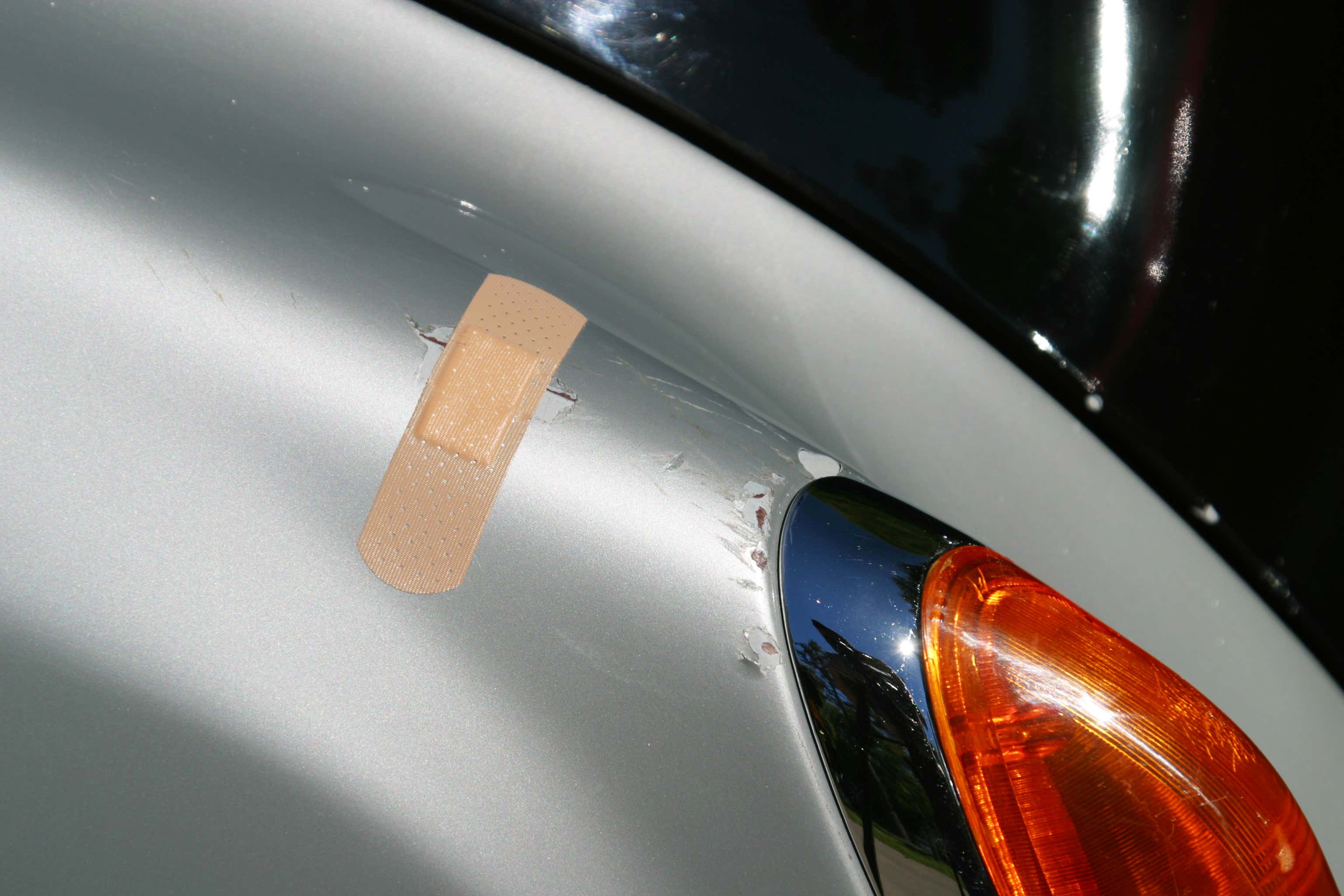 Band-Aid being used to cover a scratch on side of a silver car 带援助用来覆盖一辆银行侧面的划痕