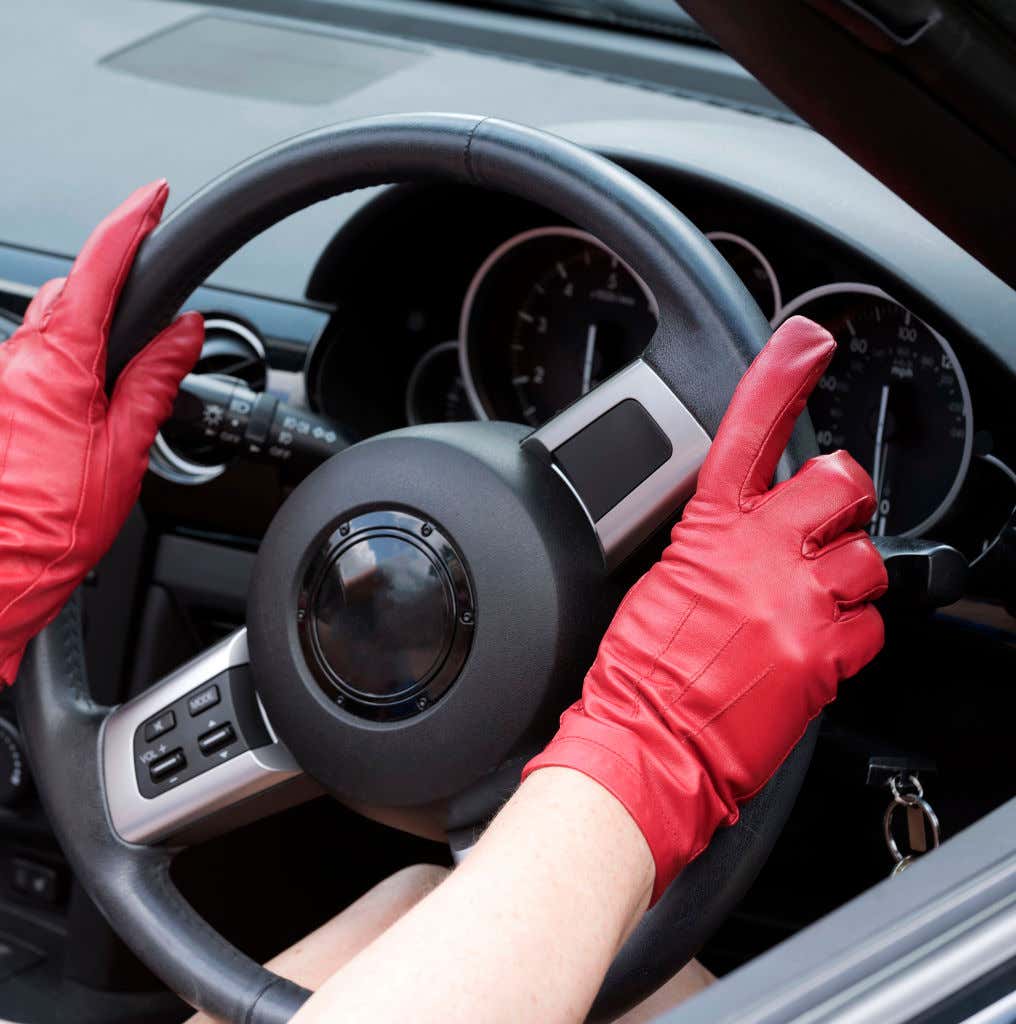 Red leather driving gloves placed on a steering wheel. 红色皮革驾驶手套放在方向盘上。