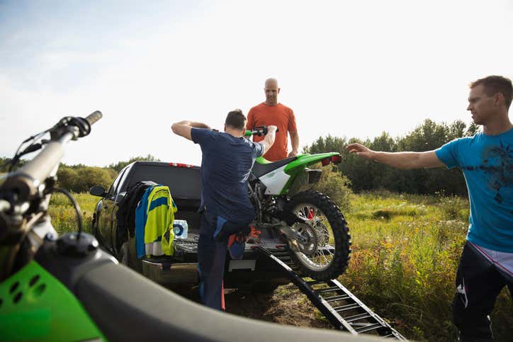 People loading a dirt bike into a truck with a ramp. 人们将污垢自行车装入与舷梯的卡车。