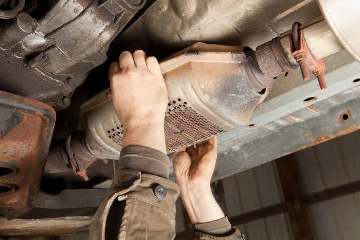 Hands of a mechanic visible in the process of changing an old catalytic converter with rusted parts 更换生锈零件的旧催化转化器时,可以看到机械师的手