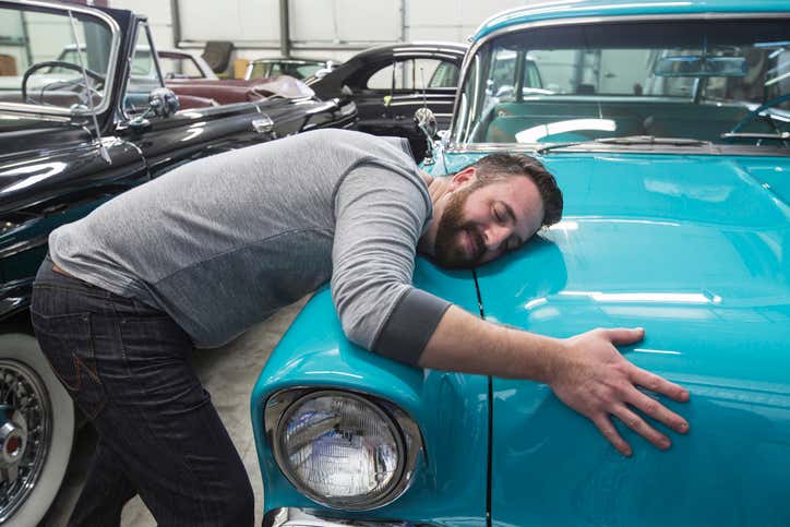 A man hugging his antique vehicle. 一个男人抱着他的古董车。