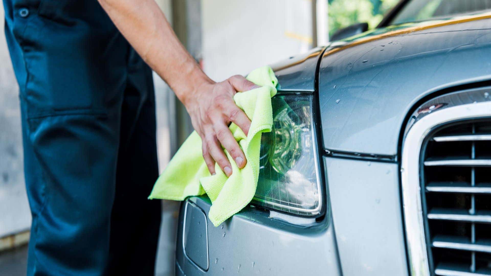 A man wiping away water on a headlight. 一个人在车灯上擦掉水。