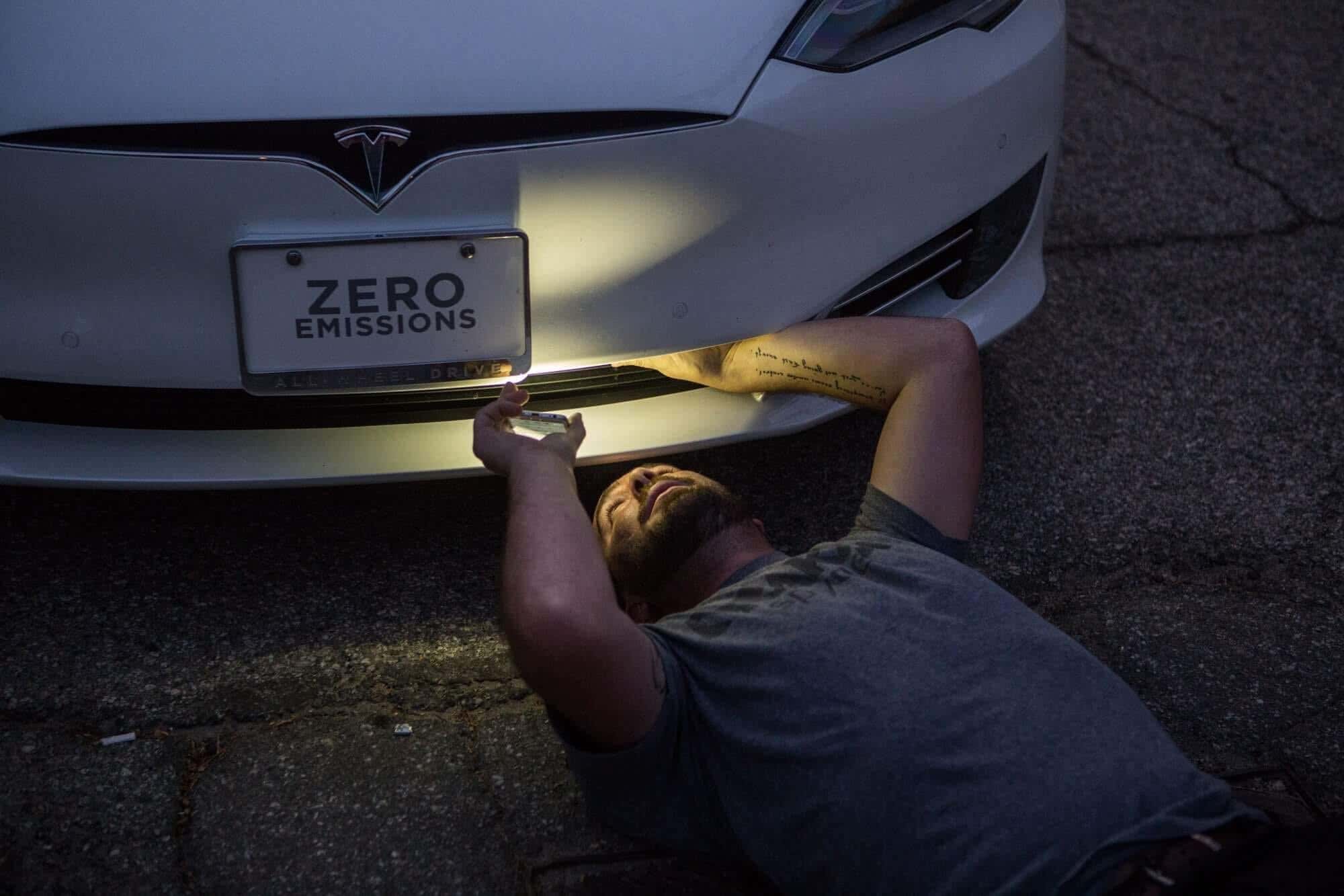 A guy looks underneath a Tesla Model S. 一个家伙看起来在特斯拉模型S。