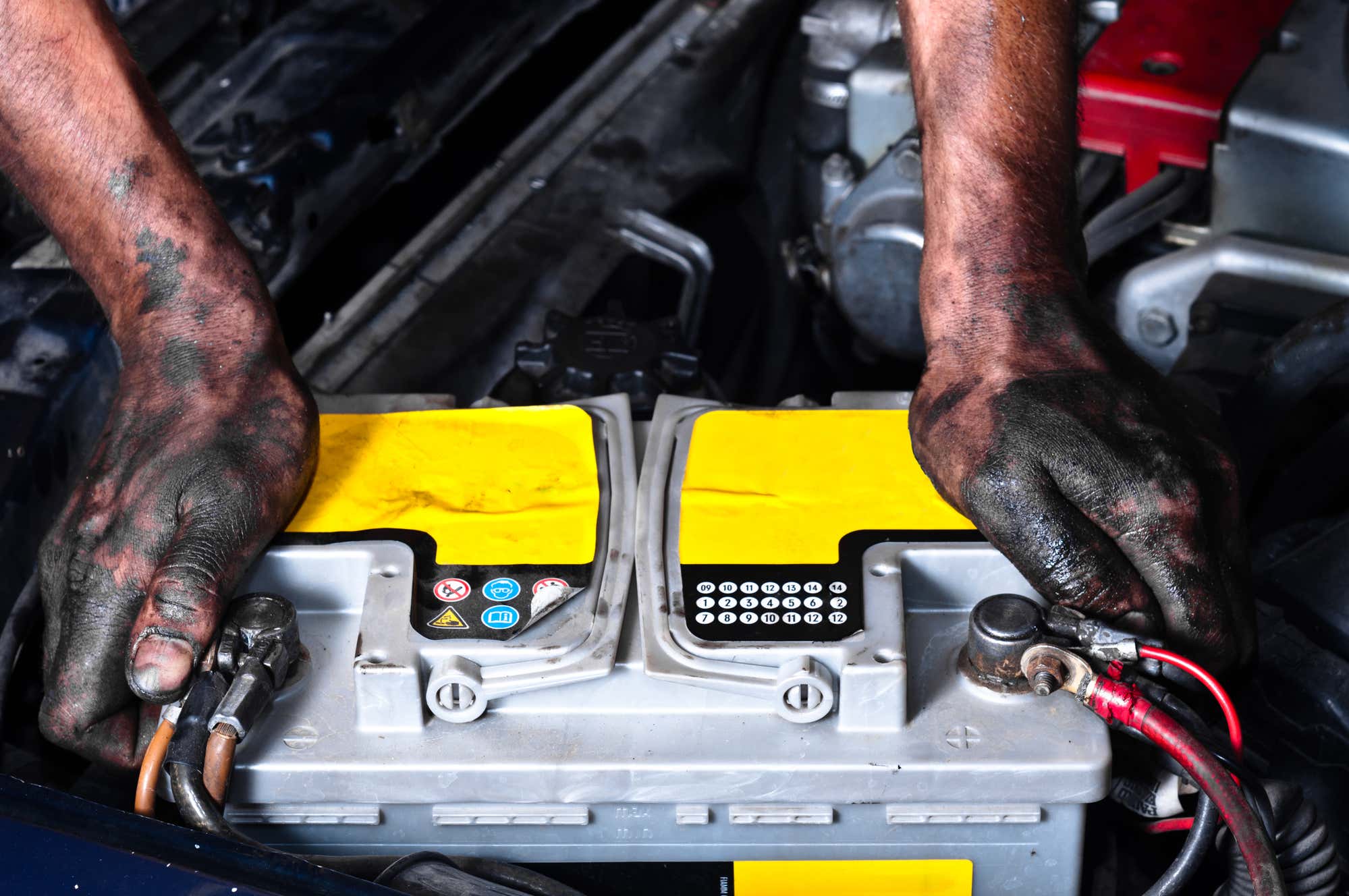 Dirty hands grip a battery in the engine bay. 肮脏的手握着发动机舱里的电池。