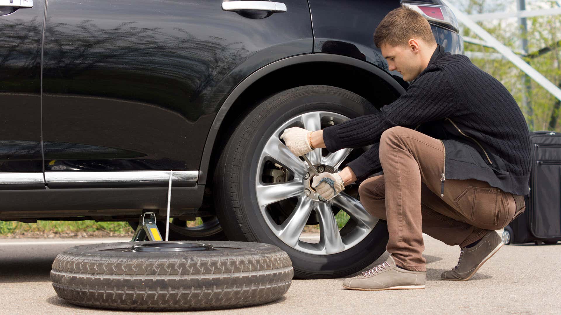 A man wrenches on lug nuts before installing a spare tire. 一个人在安装备用轮胎前要拧上螺母。