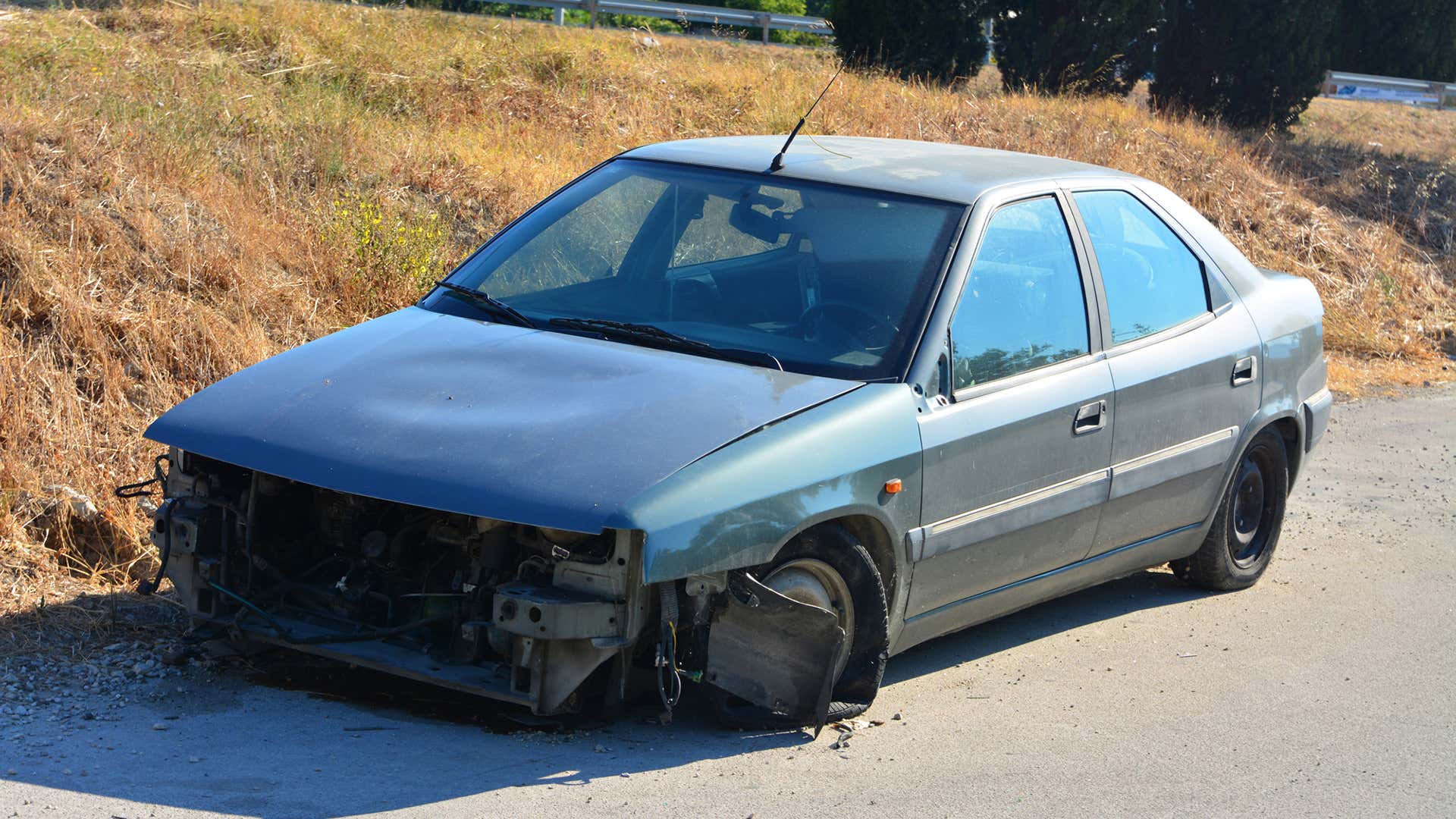 A busted car with no front end sits on the side of the road. 一辆没有前端的破车停在路边。