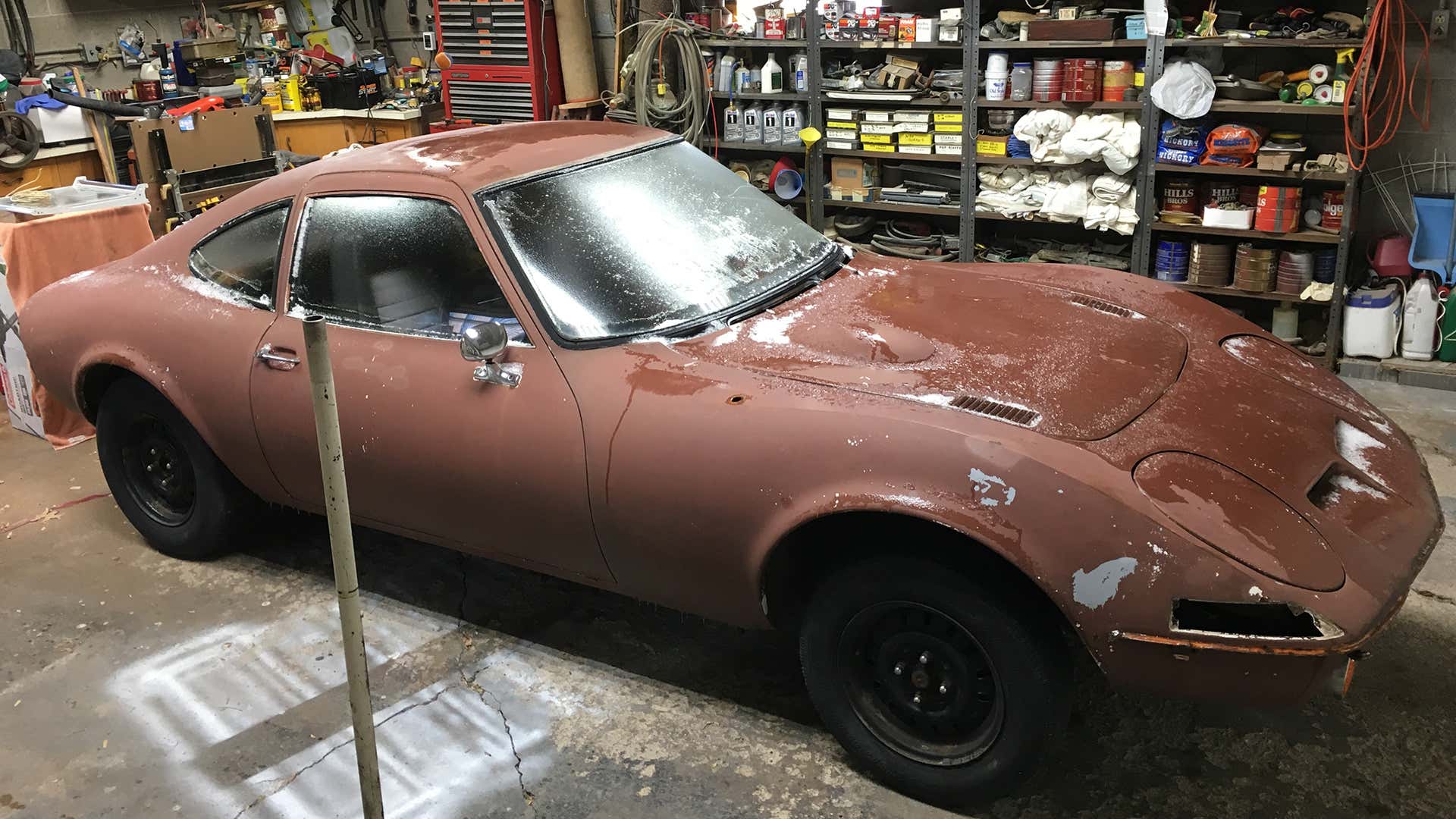 A brown Opel GT in a chaotic garage. 一个棕色的opel gt在混乱的车库中。