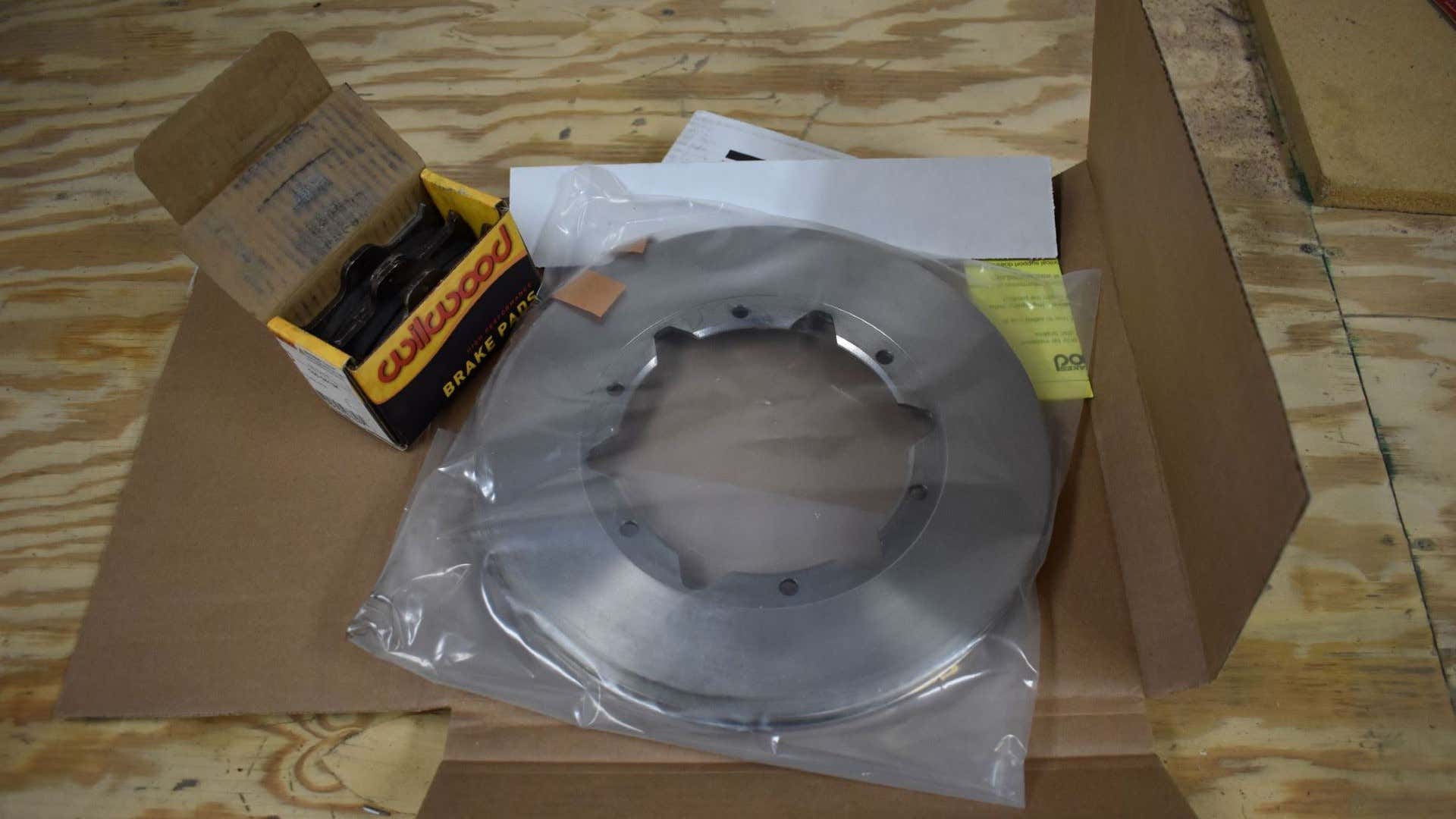 New brake pads and brake rotors in a box on a wooden table. 新刹车片和刹车转子装在木桌上的盒子里。