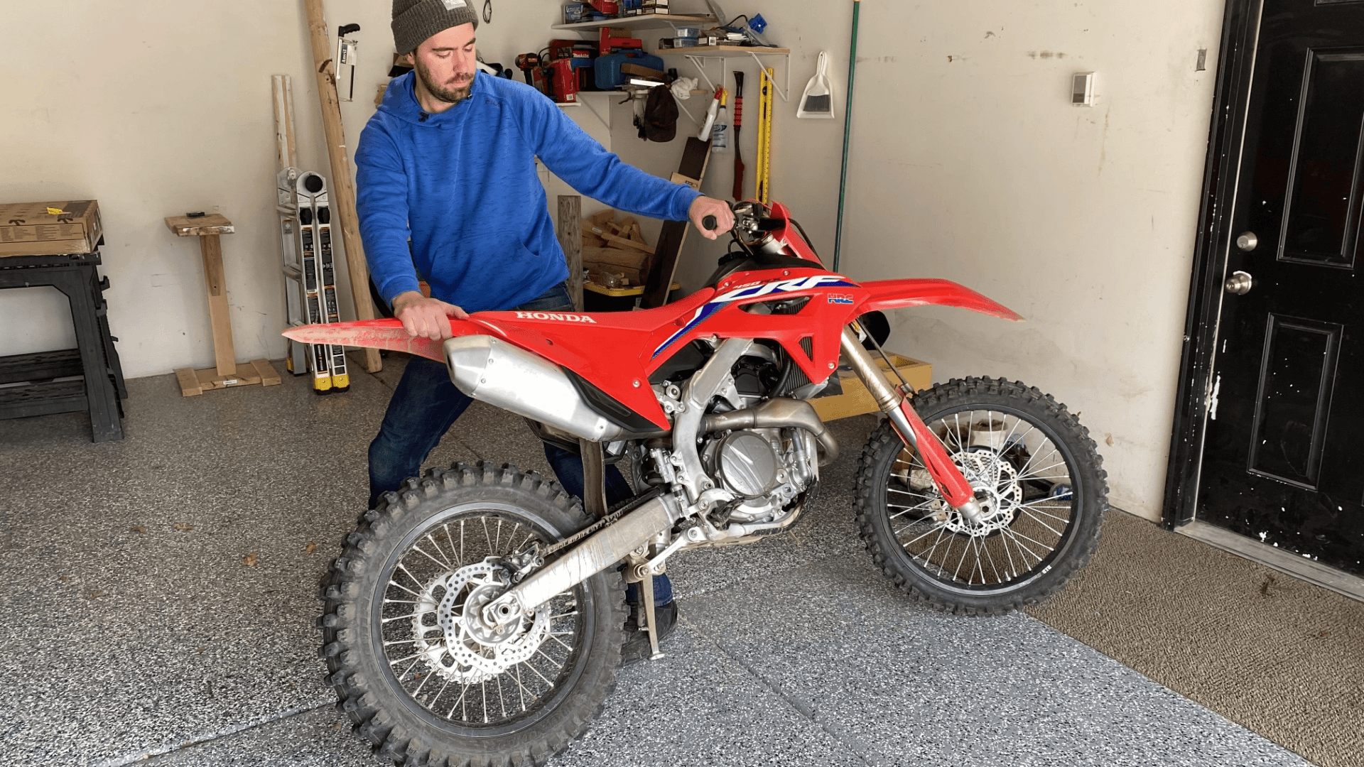 一名男子在车库内的支架上旋转一辆红色本田dirtbike。
